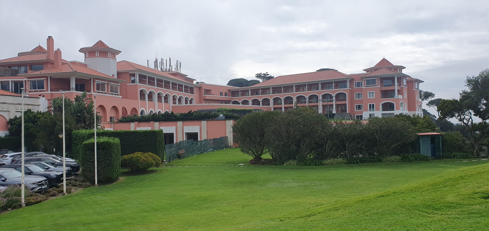 Pastellrosa Hotelanlage des Penha Longa Resorts mit gepflegtem Rasen und Gartenanlage unter bewölktem Himmel.