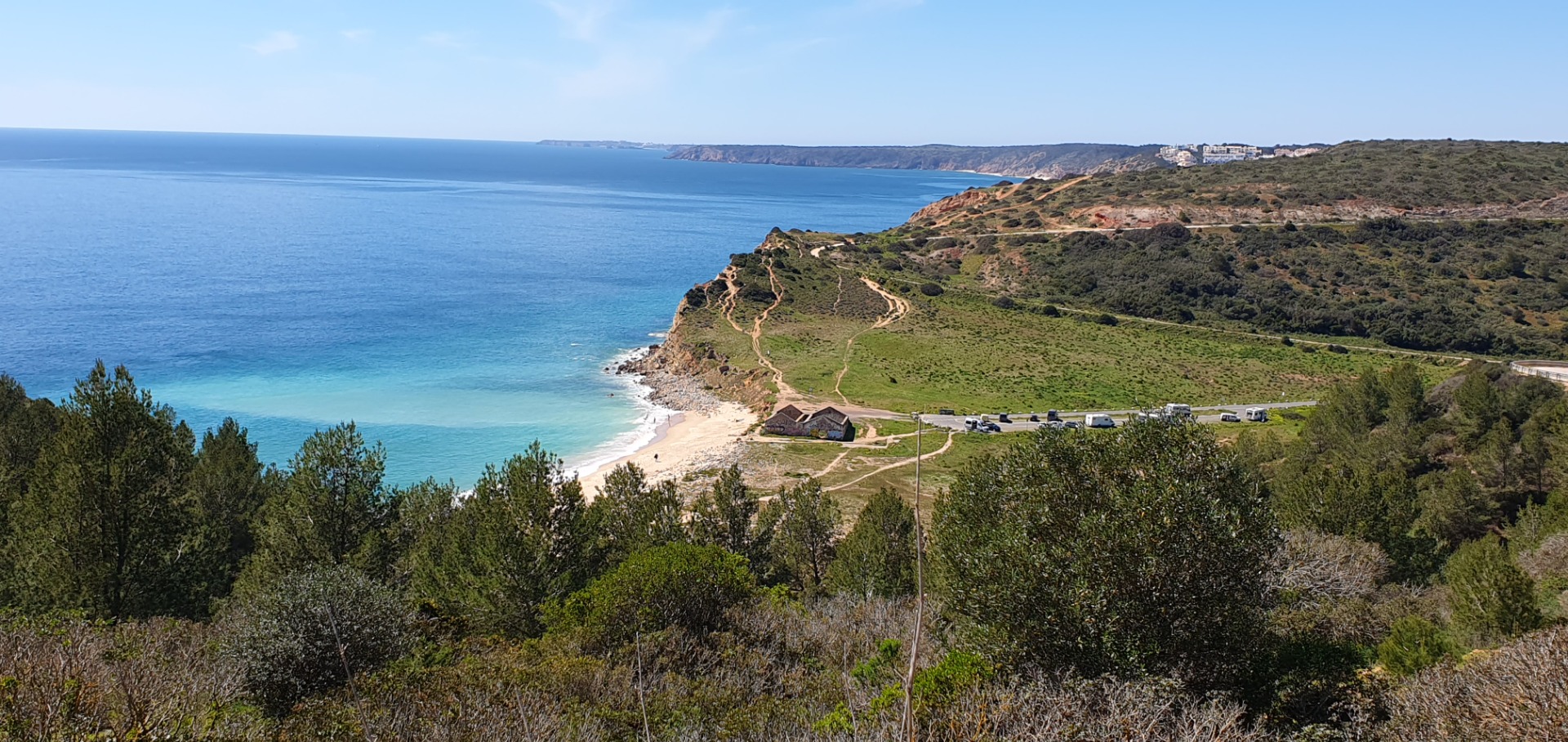 Blaue Küste der West Algarve mit Sandstrand, grünen Klippen, schmalen Wegen und geparkten Wohnmobilen am Meer.