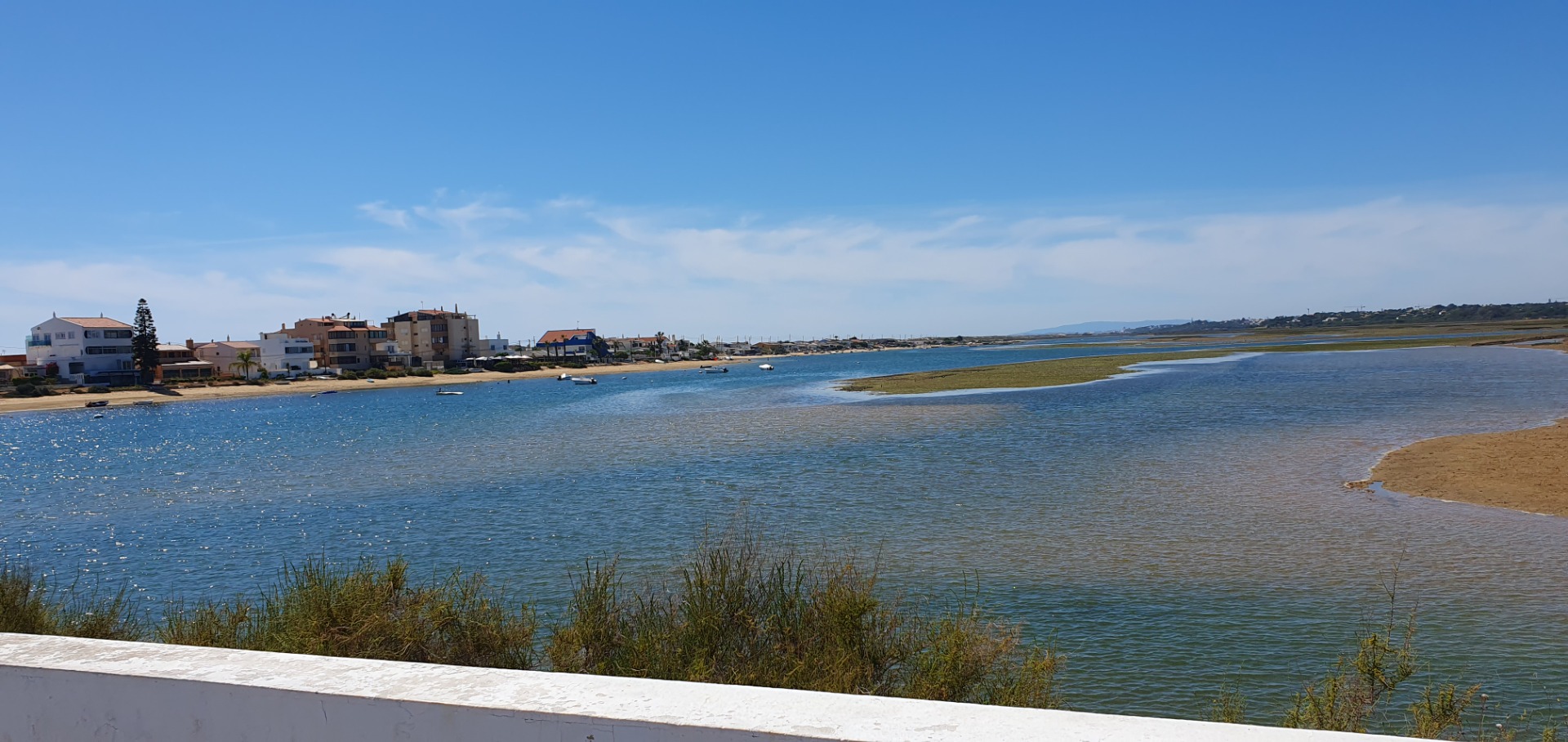 Bucht mit blauem Wasser, Sandstrand, kleinen Booten und Küstenhäusern unter klarem Himmel.