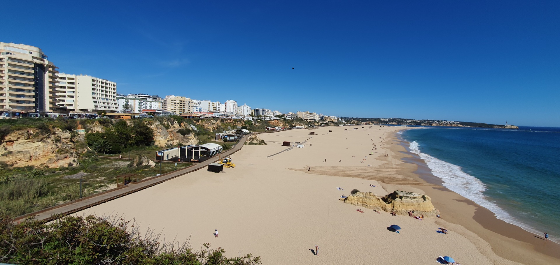 Breiter Sandstrand mit Spaziergängern, Wellen am Meer und mehrstöckigen Hotels entlang der Küste.
