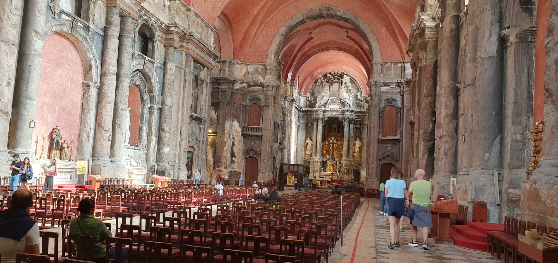 Innenraum einer Kirche mit hohen Bögen, roten Wänden, vielen Sitzreihen und Besuchern vor dem Altar.