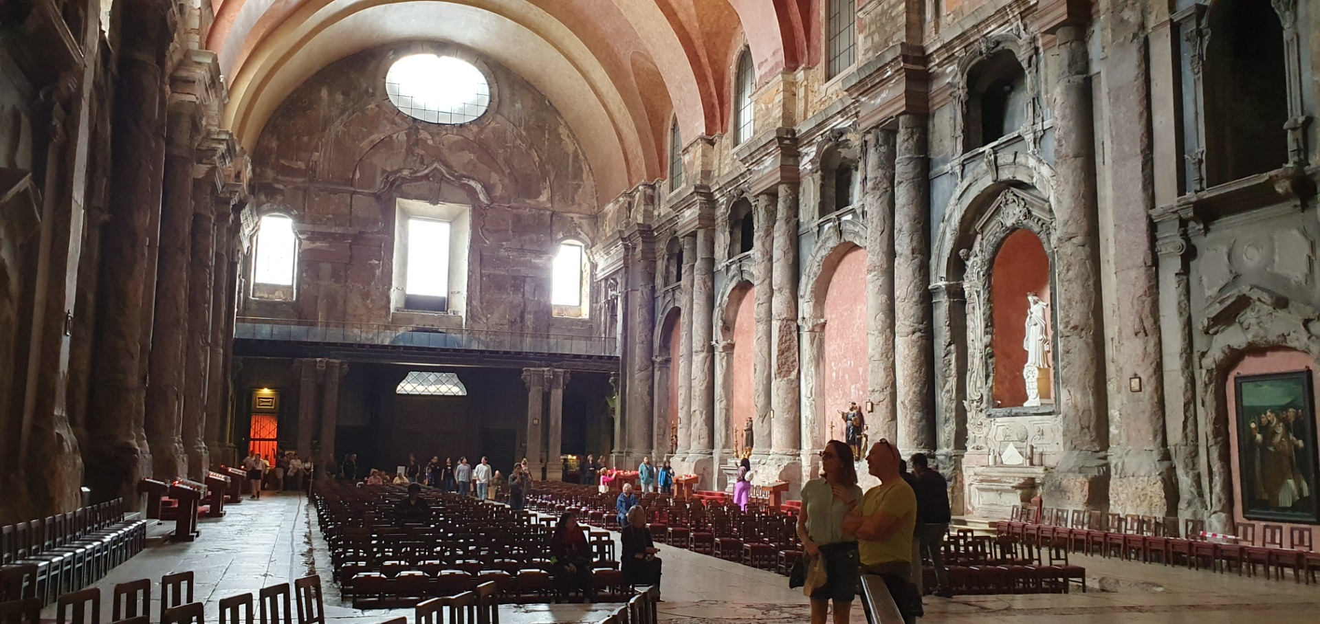 Innenansicht einer historischen Kirche mit hohen Rundbögen, Säulen, Bänken und beleuchtetem Altarraum.