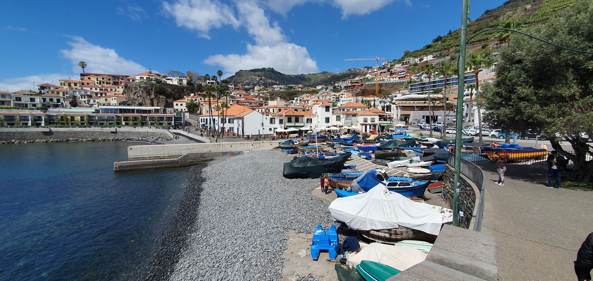 Camara dos Lobos - Madeira - Vista costeira com barcos de pesca atracados, casas coloridas e montanhas sob céu azul com nuvens.