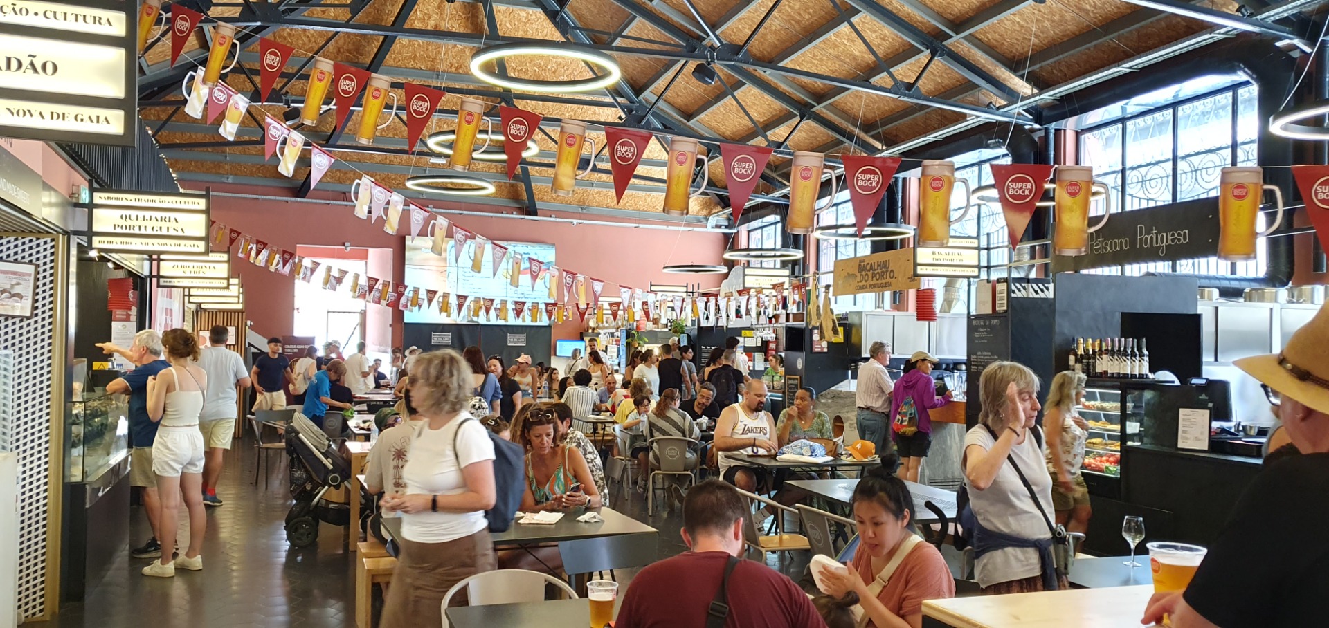 Market - Vila Nova de Gaia -Porugal - Busy restaurant interior with diners, beer mugs overhead, and colorful banners under a wooden vaulted ceiling.