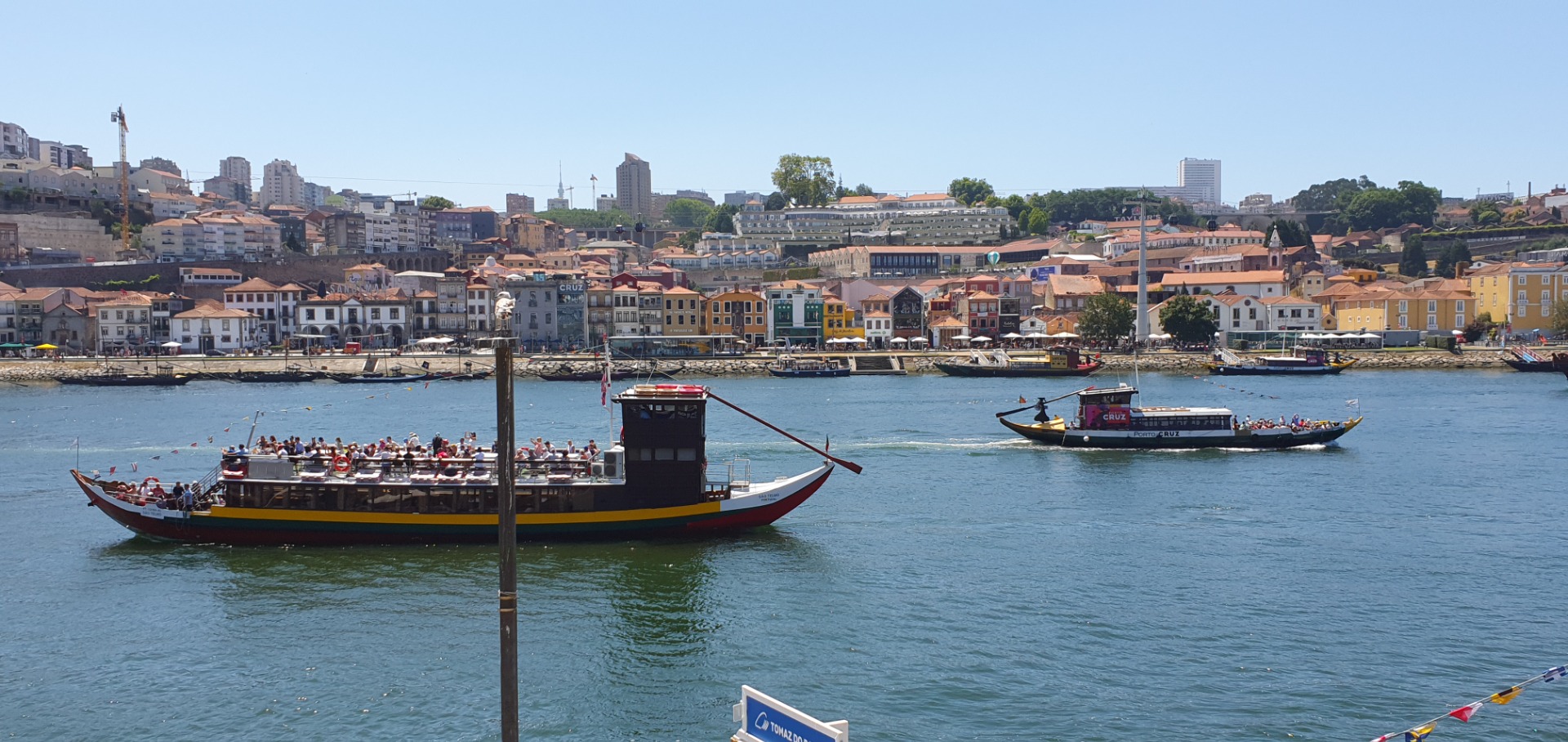 Douro River - Two passenger boats cruise on a river, with crowds onboard and a colorful riverside city skyline behind.