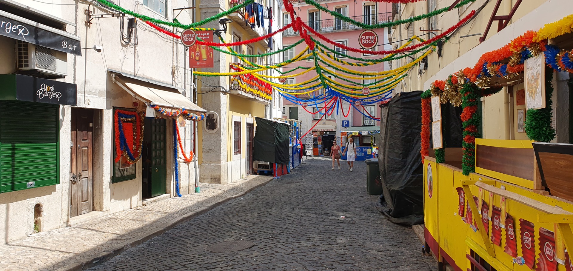 Alfama -Lisbon - Portugal - Narrow cobblestone street decorated with colorful garlands, flags, and a yellow beer cart.